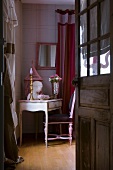 View through open wooden door with glass panels of delicate, antique writing desk with pink, feminine accessories
