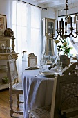 Ornate wooden chairs with woven seats and backs around festively set table below antique chandelier
