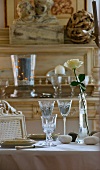 Table set in pale colours with etched glasses, pebbles and white rose; natural wood antique dresser in background