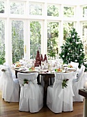 Festlich gedeckter Weihnachtstisch im Wintergarten mit Stühlen in eleganten Stoffhussen
