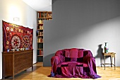 Brightly coloured throw on sofa in front of grey-painted partition in modern living room with traditional ambiance