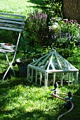 Cold frame next to garden chair and antique-style metal elements for guiding garden hose
