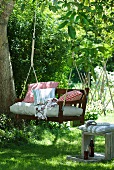 Wooden garden swing with cushions hanging from tree on ropes