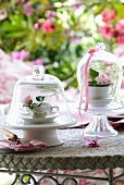 Roses in teacups under bell jars on garden table