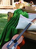 Wooden bench with blanket, cushions and guitar