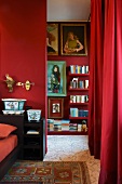 Red bedroom - open doorway next to red curtain and view of floating shelves of books on red wall