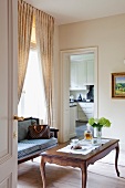 Rokoko Couchtisch und antike Sitzbank in Zimmerecke vor Fenster und Blick durch offene Tür in die Küche
