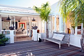 Wooden bench between palm trees on modern deck in front of Mediterranean house with open terrace doors