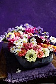 Short-stemmed, late summer garden flowers arranged in enamel dish on folded, fringed violet linen cloth