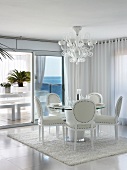 Elegante weiße Lederstühle um rundem Esstisch in modernem Esszimmer mit Glasfassade und Blick auf das Meer