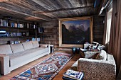 Goldgerahmtes Berglandschaftsbild in holzverkleidetem Wohnzimmer mit langer Couch und Bücherwand