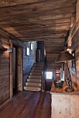 Blick vom holzverkleideten Flur mit Holzdecke und -boden in helles Treppenhaus mit Steintreppe