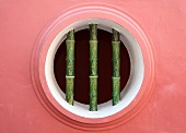 Kreisförmige Öffnung mit bambusähnlichen Gitterstäben in roter Hausfassade