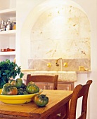 Yellow dish of tomatoes on rustic table in front of niche with rounded arch and integrated sink