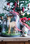 Christmas arrangement - animal ornament under bell jar and angel figurine on wooden table top in front of decorated Christmas tree