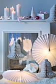 Circular paper lampshades and decorative paper bells arranged around fireplace with lit candles on mantelpiece
