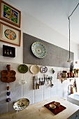 Knives and scissors on magnetic rack surrounded by colourful collectors' plates on mixture of wall tiles above improvised kitchen counter