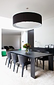 Table and chairs in black material on white rug and designer pendant lamp with circular black lampshade