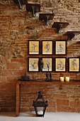 Wall console table, collection of pictures and cantilevered stairs in front of a rustic brick wall