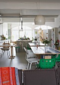 Loftähnlicher Wohnraum mit mehreren Tischen und verschiedenen Stühlen vor offener Küche