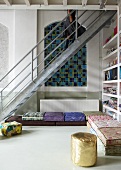 Stahltreppe vor Wand mit Rundbogen-Nischen und farbige Sitzpolster auf Boden in loftähnlicher Wohnzimmerecke