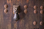 Door knocker in the shape of a hand on rusty metal door