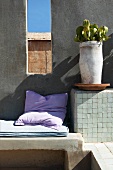 Kissen und Polster auf gemauerter Sitzbank und Pflanzentopf auf Ablage neben fensterartiger Öffnung in Wand