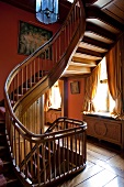 Traditional stairwell with winding wooden staircase against rust brown walls and old board floor