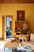 Sessel mit passendem Fussschemel im Rokokostil vor antiker Kommode in gelb getöntem Wohnzimmer eines Landschlosses
