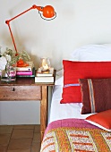 Rote Retro Tischlampe auf Nachttisch neben Bett mit roten Kissen und Tagesdecke