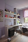 Modern work area with white fitted shelving above desk in teenager's room with lilac walls