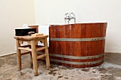 Rustic stool next to wooden bathtub in corner of spartan bathroom