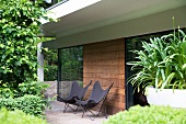 Butterfly-Sessel auf Terrasse vor Glas- und Holzwand eines zeitgenössischen Wohnhauses mit Garten