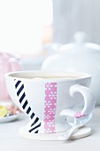 Teacup with home-made decoration of snowflake-patterned and black striped tape