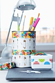 Storage pot for pens and paintbrushes made from tin can and china pot of rubber bands both decorated with patterned tape