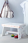 Foot stool decorated with prettily patterned tape, colourful toy cars on floor and net shopping bag hanging on wall