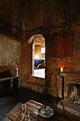 Room with fireplace in old house with sooty walls and view of bed through open arched doorway