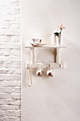 Shelf and row of hooks with cups and string of beads against white wall