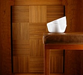 Two white bowls on bar stool against brown wooden wall