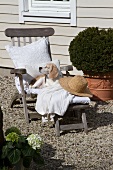 Dog snoozing on deckchair with white cushions and straw hat
