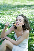 Young woman sitting outdoors, blowing bubbles, looking down