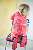 Blonde toddler girl climbing on chair, rear view