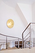 Golden wall lamp on stairwell wall and view down staircase with stainless steel balustrade