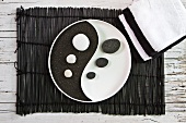 Yin and Yang dish with black pumice and white pebbles on bamboo mat