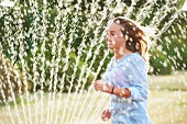 Young woman running through spray of a sprinkler