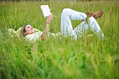 Woman lying in long grass with book