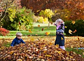 Children playing with fallen autumn leaves in park