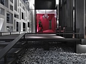 Empore mit Treppe aus dunklem Holz auf Kieselsteinbelag und Blick in offenen Vorraum auf Raumteiler und rote Wand