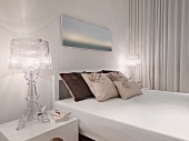 Weisses Schlafzimmer mit Kissenstapel neben Nachttischlampen aus transparentem Acrylglas im Retrostil