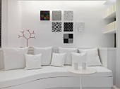 Geschwungenes Sofa mit Kissen vor Wand mit modernen Bildern und Beistelltisch in Weiß